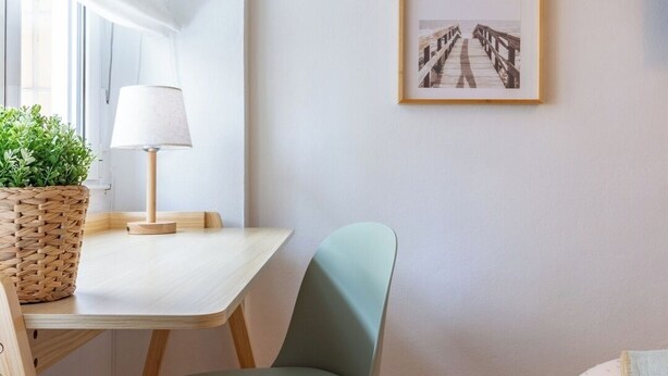 Una habitación con un escritorio de madera, una silla verde, una lámpara y dos cuadros en la pared.