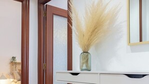 Un pasillo con una puerta de madera, una consola blanca con un jarrón de plumas de pampa y un espejo en la pared.