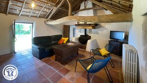 A rustic interior with a high wooden ceiling, a leather sofa, a coffee table, wicker chairs, and a television.