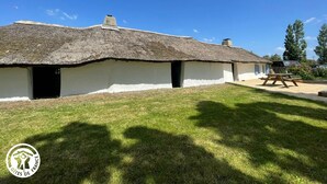 A traditional thatched-roof house with a white exterior, a chimney, and a small porch area.