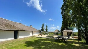 A rural setting with thatched-roof cottages, a picnic area, and a clear blue sky.