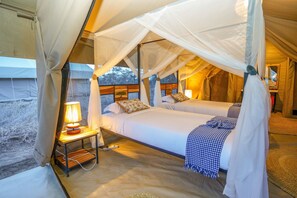 A tented accommodation with two beds, a bedside table with a lamp, and a canopy bed. - Malaika Mara River Migration Camp (Serengeti)