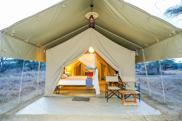 A tent with a bed, a table, and a chair inside. - Malaika Mara River Migration Camp (Serengeti)