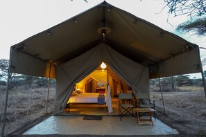 A tent with a bed, a hanging light, and a table with chairs. - Malaika Mara River Migration Camp (Serengeti)