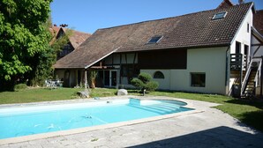 A residential property with a swimming pool, a covered patio, and a two-story house with a tiled roof.