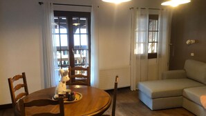 A living room with a wooden dining table, two chairs, a sofa, and a window with curtains.
