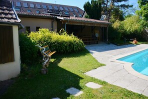 Um imóvel residencial com piscina, varanda coberta e jardim com um banco.