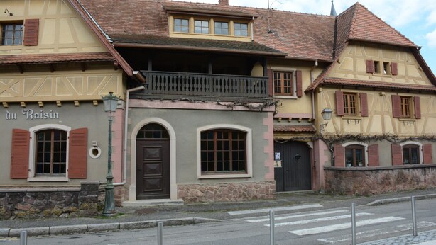 A traditional half-timbered building with a balcony, a stone wall, and a sign that reads 'du Raisin.'
