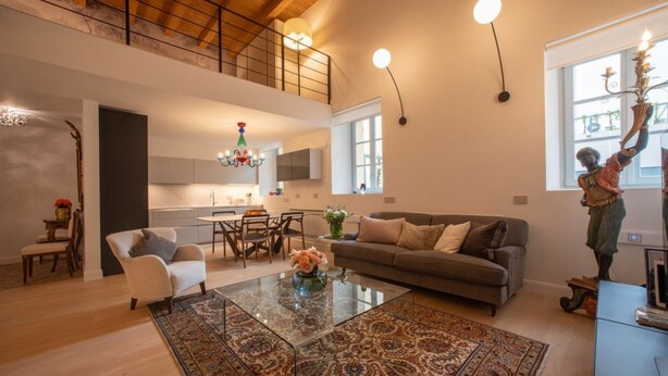 A spacious living area with a high ceiling, a dining table, a sofa, and a decorative statue.