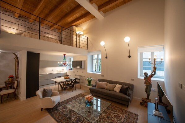 A spacious living area with a high ceiling, a dining area, a kitchen, and a balcony.