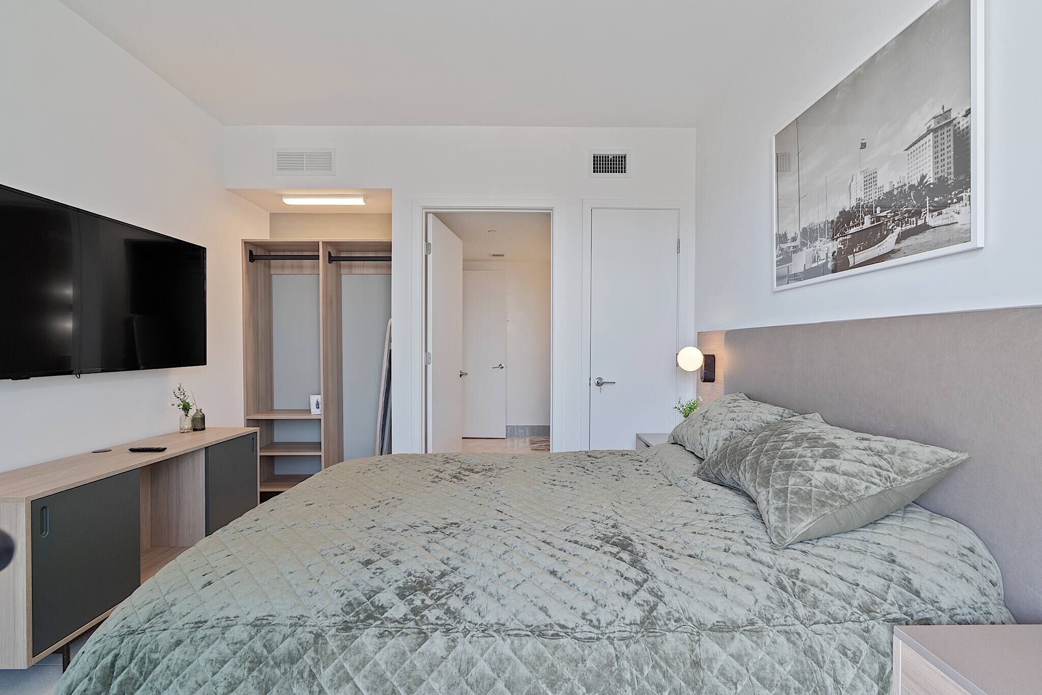 A modern hotel room with a large bed, a flat-screen TV, a wardrobe, and a framed picture on the wall.
