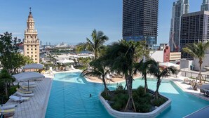 A rooftop pool with palm trees, lounge chairs, and a view of the cityscape including a historic tower and modern buildings. - Luxury Corner 2bdcity & Bay Viewsamazing Sunsets (Miami)