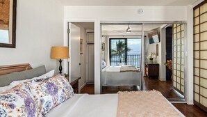Una camera da letto con un letto, un comodino, una lampada e vista sull'oceano attraverso una porta scorrevole.