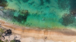 Vista aerea di una spiaggia con acque cristalline turchesi, spiaggia sabbiosa e vegetazione rada.