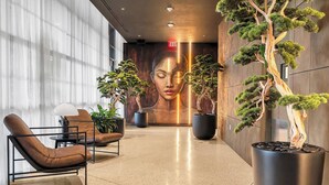 Eine moderne Lobby mit einer großen Wandmalerei, Bonsai-Bäumchen in Töpfen, Ledersesseln und einem minimalistischen Design.