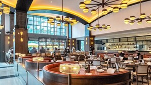 A spacious restaurant with high ceilings, modern lighting fixtures, and a bar area.