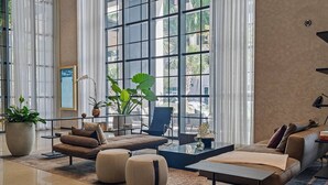 A spacious living area with a large window, a sofa, ottomans, a coffee table, and potted plants. - Luxury 1BR Penthouse, Bay & City Views Downtown (Miami)