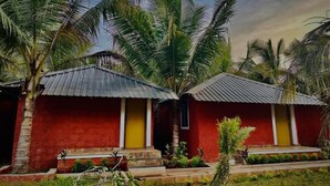 A red building with a yellow door, surrounded by palm trees and greenery. - Ocean Paradise Beach Homestay (Karwar)