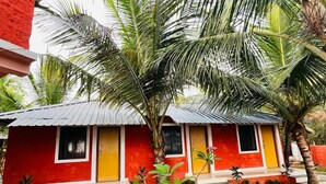 A red and yellow building with a corrugated metal roof, surrounded by palm trees and small plants. - Ocean Paradise Beach Homestay (Karwar)
