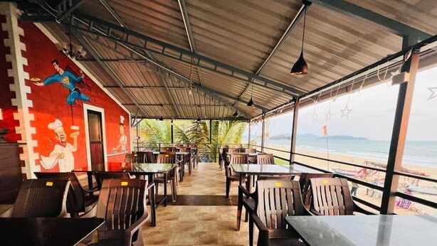 An outdoor restaurant with tables and chairs, a mural on the wall, and a view of the beach. - Ocean Paradise Beach Homestay (Karwar)