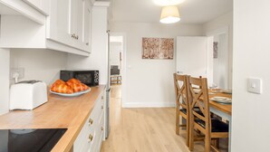 A modern kitchen with white cabinets, a wooden countertop, a black stove, a microwave, and a toaster. There is a dining area with a wooden table and chairs. - 17 Clifden Court getaway with free parking (Clifden)