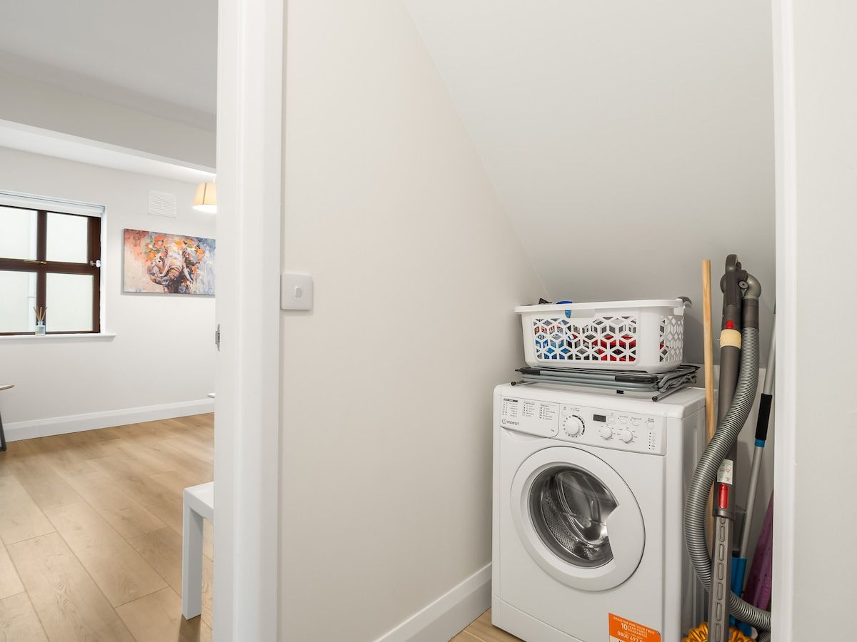 A laundry area with a washing machine, a basket, and a vacuum cleaner.