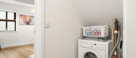 A laundry area with a washing machine, a basket, and a vacuum cleaner.