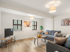 A modern living room with a flat-screen TV, a sofa, a coffee table with fruit, and artwork on the walls. - 17 Clifden Court Townhouse W/ Parking (Clifden)