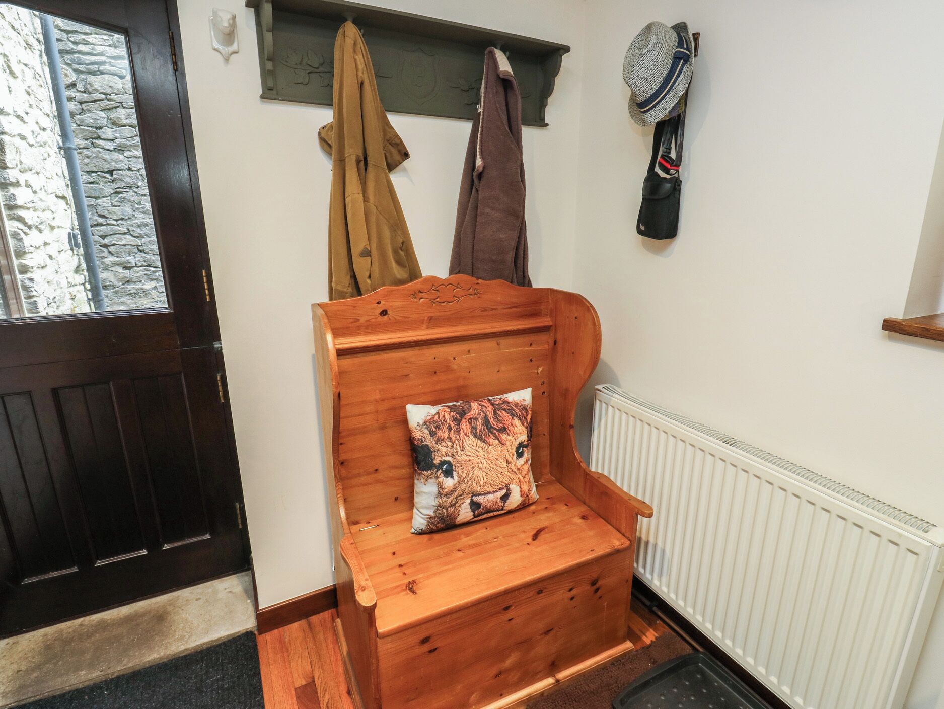 A wooden bench with a cushion, a coat rack with jackets, and a hat hanging on the wall.