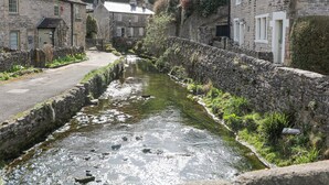 Ein schmaler Wasserkanal, gesäumt von Steinhäusern mit traditioneller Architektur, einer gepflasterten Straße und einer Steinmauer.