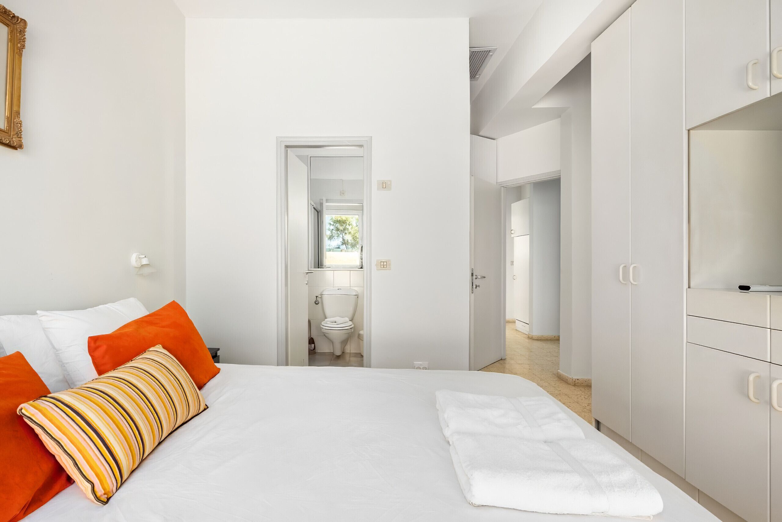 Una camera d'albergo con un letto, pareti bianche, una porta che conduce al bagno e un armadio.