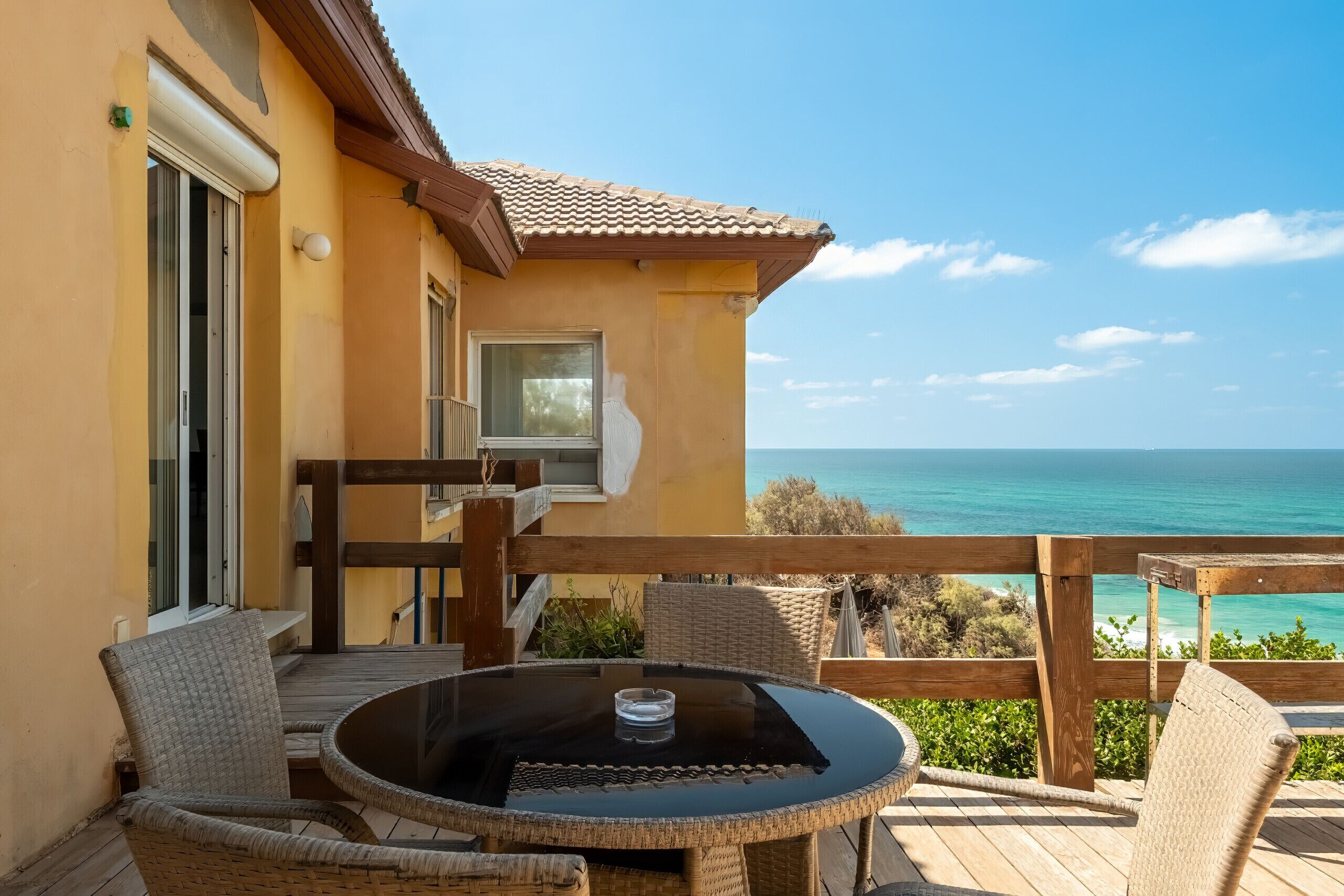 A balcony with wicker furniture, a glass table, and a view of the ocean.