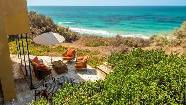 Un patio con mobiliario de mimbre y una sombrilla, con vistas a la costa.
