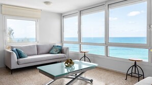 Una sala de estar moderna con un sofá, una mesa de centro de vidrio y vistas al océano a través de amplios ventanales.