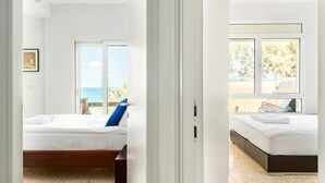 Habitación de hotel con cama, ventana con vista al mar y puerta que da a otra habitación.