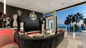Un soggiorno moderno con un'ampia televisione a schermo piatto, divani scuri, vasi decorativi e vista sull'oceano.