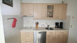 Eine kompakte Küche mit hellen Holzschränken, einem Edelstahl-Geschirrspüler, einem Gasherd und einer Kaffeemaschine.