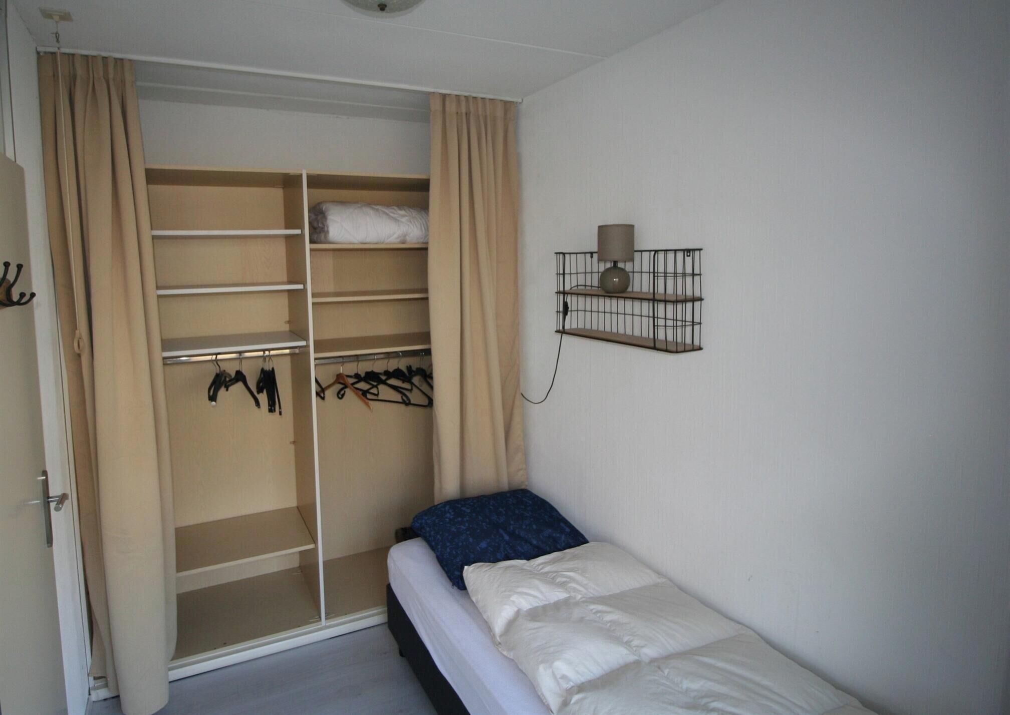 Quarto com cama, guarda-roupa e estante com abajur.