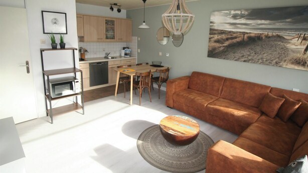 Eine moderne Küche mit Holzschränken, eine Essecke mit Tisch und Stühlen, ein braunes Ledersofa und ein großes Gemälde mit einer Strandansicht.