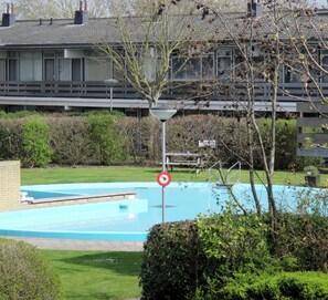 Uma área residencial com piscina, placa de proibição de estacionamento e um edifício com telhado cerâmico ao fundo.