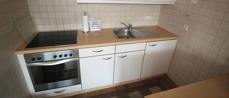 Une cuisine de taille réduite, équipée d’une cuisinière, d’un four, d’un évier et de meubles blancs.