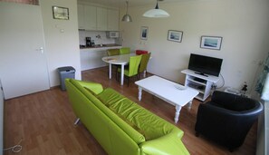 Un espace de vie compact comprenant un canapé, une table à manger, des chaises, un téléviseur et un coin cuisine.
