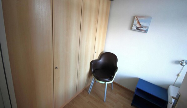 Une pièce avec une armoire en bois, une chaise noire, une petite table et un tableau accroché au mur.