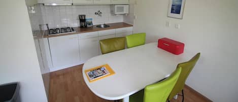A compact kitchen with white cabinets, a microwave, a coffee maker, and a dining table with green chairs.
