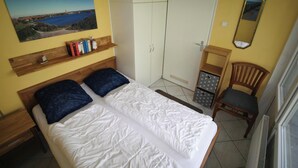 Un dormitorio con dos camas, un armario, una silla, una estantería con libros y un cuadro en la pared.