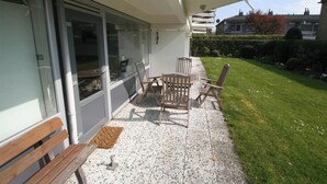 Un patio con una mesa, sillas, un banco y una puerta que da a un espacio cubierto.