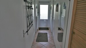 Un pasillo con suelo de baldosas, un felpudo y una puerta con reja de metal.