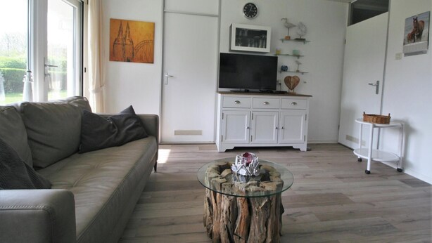 Una sala de estar con sofá, una mesa de centro de vidrio, televisor y mueble.