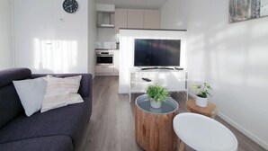 A modern living room with a sofa, a coffee table, a TV, and a kitchen area.
