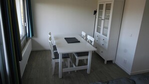 A small, white room with a table and chairs, a cabinet with glass doors, and a window with curtains.